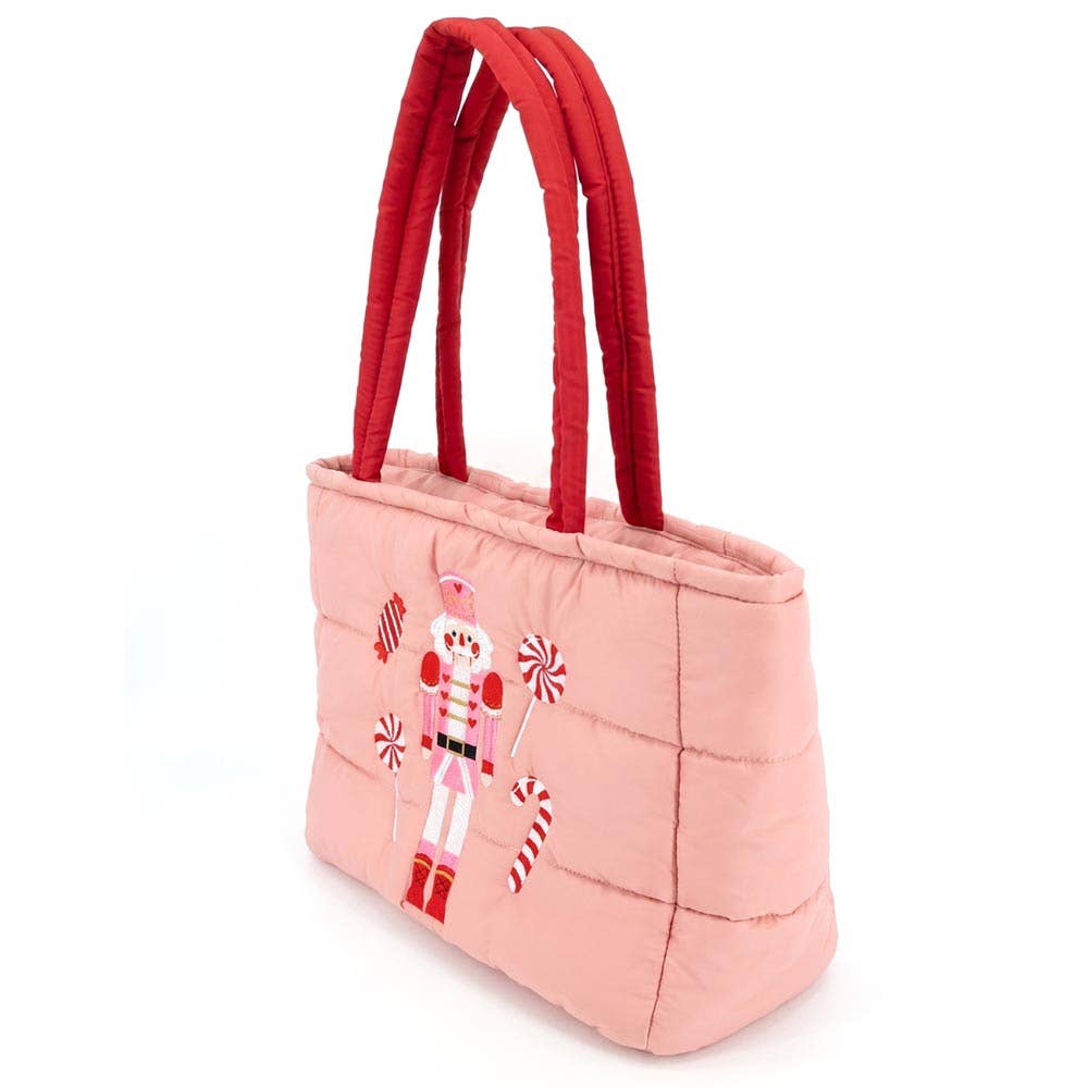 Faire Nutcracker Holiday Candy Cane Embroidered Quilted Shoulder Tote Bag. It has a red strap, the bag is pink with nutcracker, candy cane, lollypops, and candy on it.