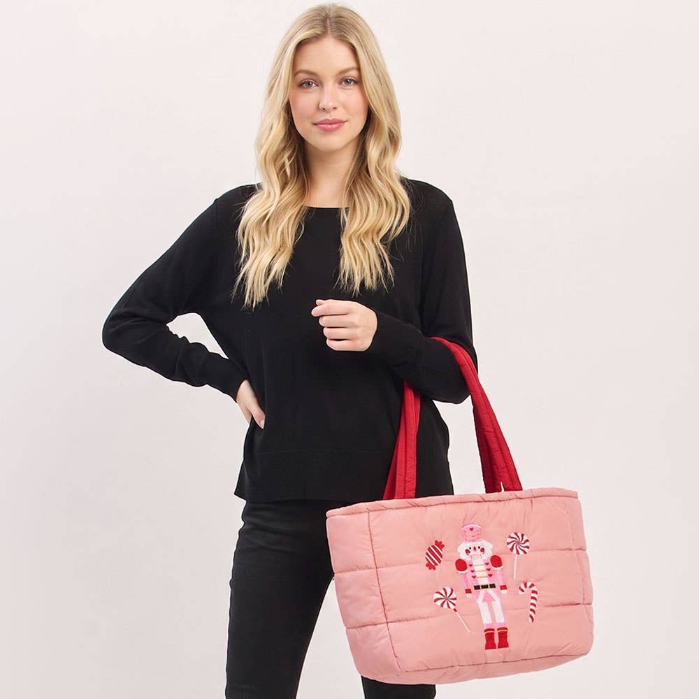 Faire Nutcracker Holiday Candy Cane Embroidered Quilted Shoulder Tote Bag. It has a red strap, the bag is pink with nutcracker, candy cane, lollypops, and candy on it.